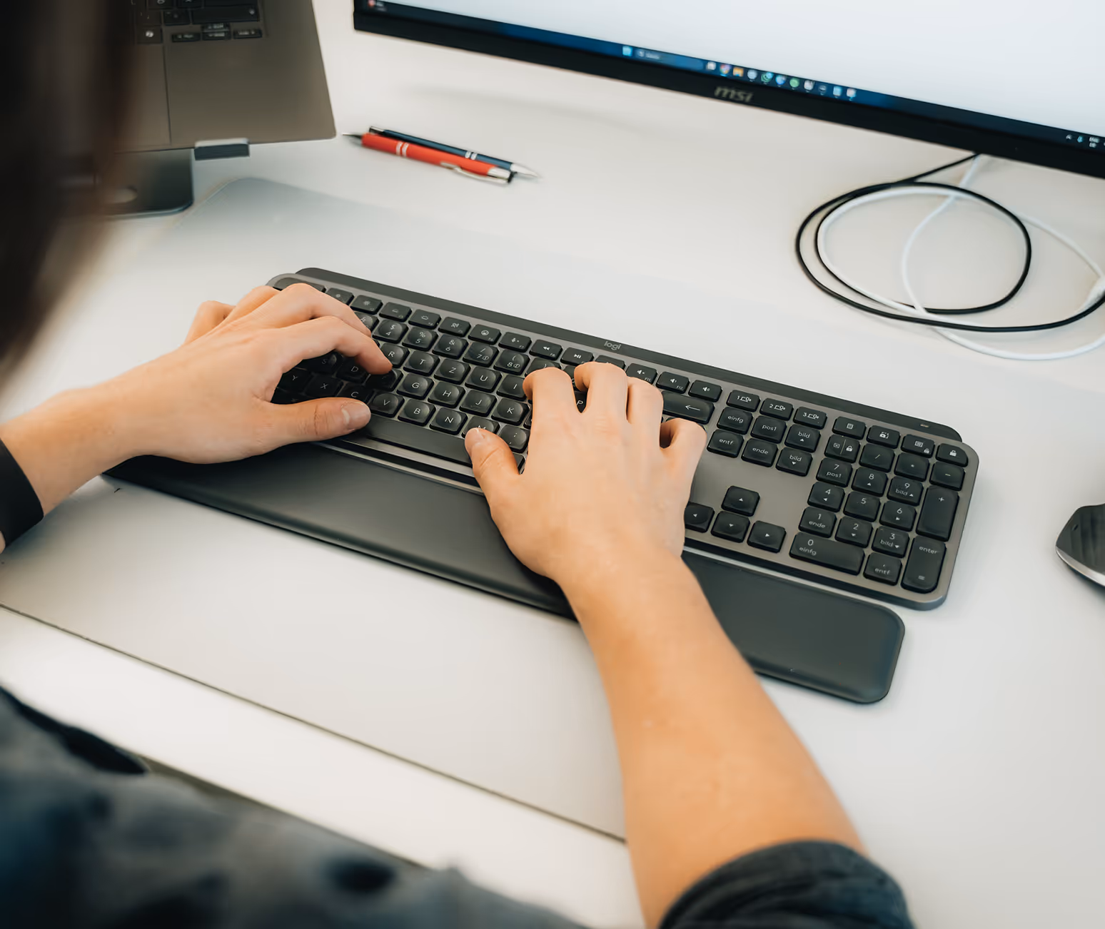 Zwei Hände tippen an einer Tastatur am Schreibtisch im FourLead-Büro